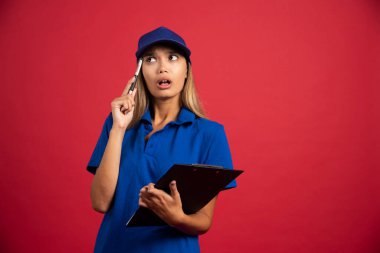 Mavi üniformalı düşünceli bir kadın elinde not panosu ve kalemle poz veriyor. Yüksek kalite fotoğraf