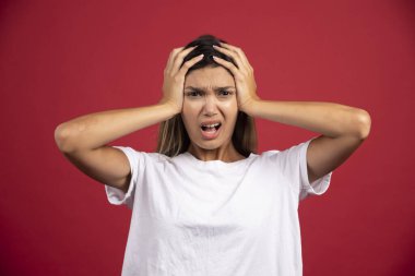 Genç bir kadın kırmızı arka planda kafasına dokunuyor. Yüksek kaliteli fotoğraf.