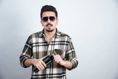 Gözlüklü genç adamın beyaz duvarda siyah bardak açtığı fotoğraf. Yüksek kalite fotoğraf