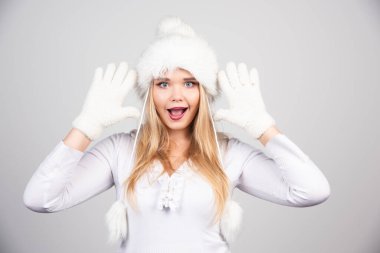 Kışlık kıyafetli sarışın kadın gri arka planda şaşırmış gibi davranıyor. Yüksek kalite fotoğraf