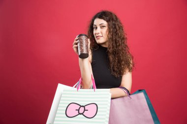 Bardaklı kadın kırmızı arka planda alışverişlerini gösteriyor. 