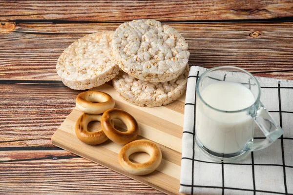 Round biscuits, rice cakes, and glass of milk on wooden table. High quality photo