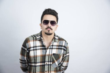 Beyaz duvarda gözlük takan yakışıklı sakallı bir adam resmi. Yüksek kalite fotoğraf