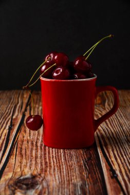 Siyah arka planda ahşap bir kasede kırmızı kirazlar..