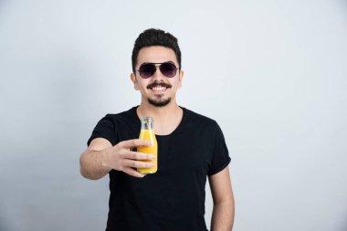 Güneş gözlüklü yakışıklı adamın fotoğrafı. Kameraya portakal suyu ile cam şişeyi gösteriyor. Yüksek kalite fotoğraf
