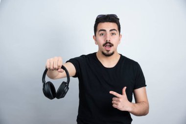 Esmer adam beyaz duvara karşı duran ve kulaklıkları işaret eden bir model. Yüksek kalite fotoğraf