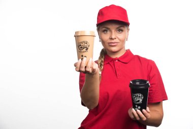 Kırmızı üniformalı kadın elinde beyaz arka planda iki fincan kahve tutuyor. 