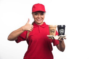 Kadın kurye elinde iki fincan kahve tutuyor ve beyaz arka planda başparmak kaldırıyor. Yüksek kalite fotoğraf