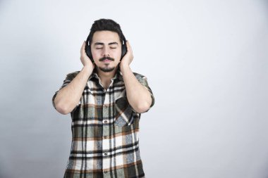 Kulaklıklı yakışıklı bir adamın beyaz duvarda şarkı dinlediği bir fotoğraf. Yüksek kalite fotoğraf