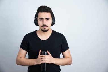 Kulaklıklı esmer adam beyaz duvara karşı bardak tutuyor. Yüksek kalite fotoğraf