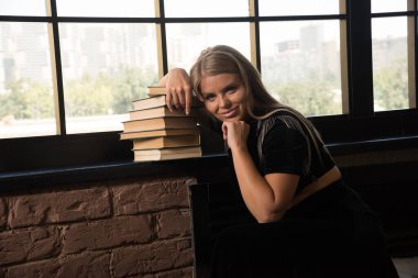 Pencerenin yanında kitaplarla poz veren genç bir kadın