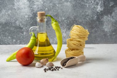 Çiğ makarna yuvaları, bir şişe zeytinyağı, biber taneleri ve sebzeler beyaz masada. Yüksek kalite fotoğraf