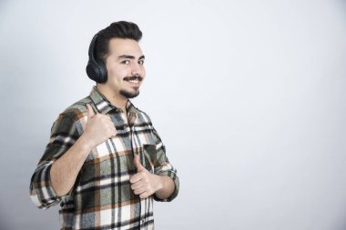 Beyaz duvardan müzik dinleyen kulaklıklı yakışıklı bir adam resmi. Yüksek kalite fotoğraf