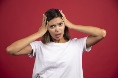 Genç bir kadın kırmızı arka planda kafasına dokunuyor. Yüksek kaliteli fotoğraf.