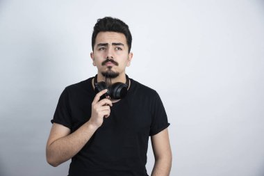 Esmer adam, kulaklıkla durup beyaz duvara karşı poz veriyor. Yüksek kalite fotoğraf