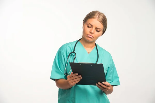 青い制服を着た金髪の女医が領収書を持って丁寧にチェック 高品質の写真 — ストック写真