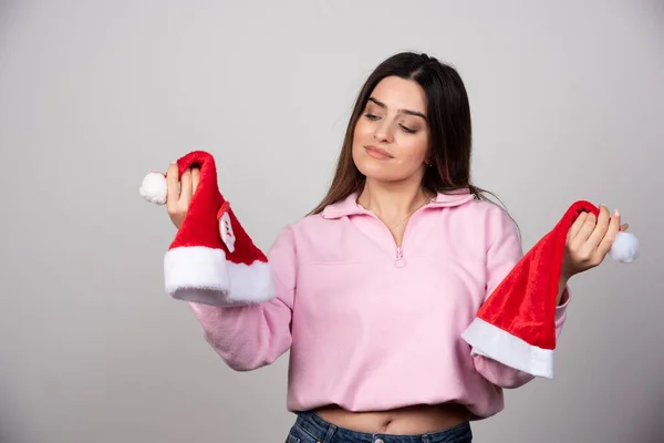 Eine Junge Frau Betrachtet Die Hüte Des Weihnachtsmannes Und Posiert — Stockfoto