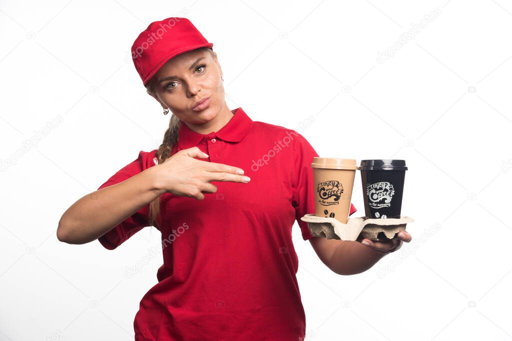 Woman courier pointing her fingers at two cups of coffees on white background. High quality photo