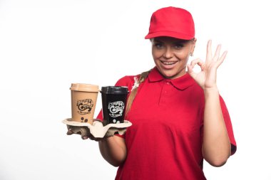 Şapkalı kadın jest yapıyor ve elinde beyaz arka planda kahve fincanları tutuyor. 