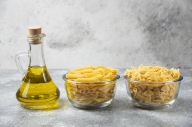 İki kase çiğ makarna ve mermer zemin üzerinde bir şişe zeytin yağı olan farfalle makarna. Yüksek kalite fotoğraf
