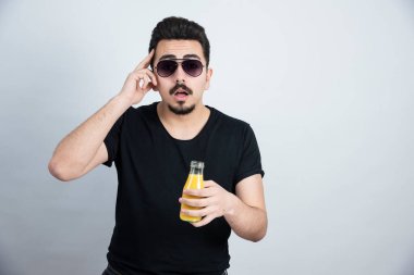 Güneş gözlüklü yakışıklı modelin elinde portakal suyu şişesiyle fotoğrafı. Yüksek kalite fotoğraf