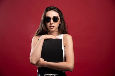 Kırmızı arka planda not defterleri tutan gözlüklü güzel bir kadın. Yüksek kalite fotoğraf