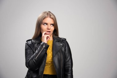 Siyah deri ceketli sarışın kız parmaklarını ağzına doğru baştan çıkarıcı bir şekilde koyar. Yüksek kalite fotoğraf