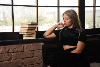 Pencerenin yanındaki kitaplara bakan genç bir kadın.