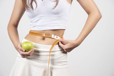 Atletik ince kadın, gri arka planda ölçülü olarak belini ölçüyor. Yüksek kalite fotoğraf