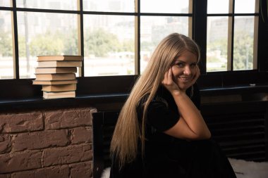 Pencerenin yanında kitaplarla poz veren genç bir kadın