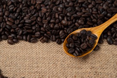 Çuval bezine saçılmış ahşap kaşıklı orta pişmiş kahve çekirdeği yığını. Yüksek kalite fotoğraf