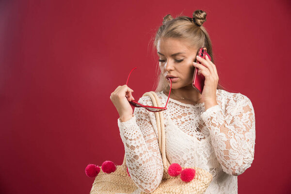 Young woman talking on phone with bag on red background