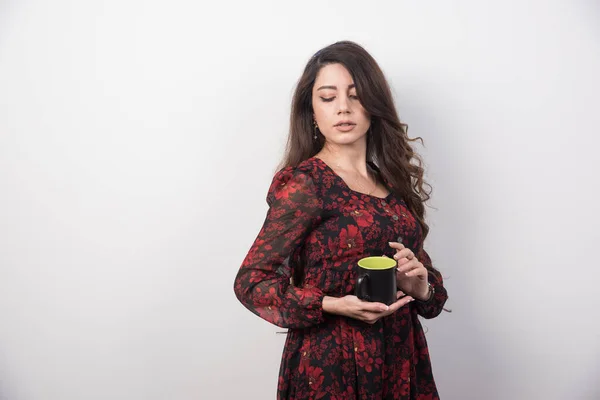 Wavy haired woman with cup of tea standing on gray background. High quality photo