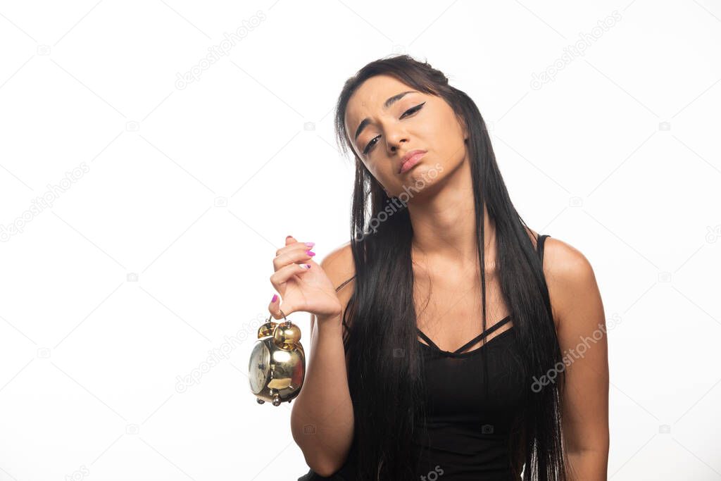 Tired woman holding an alarm clock on white background. High quality photo