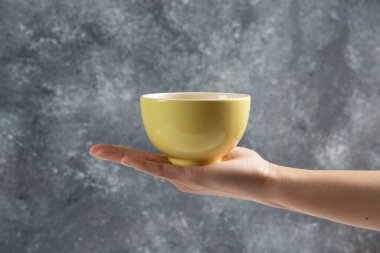 Gri arka planda sarı bir kase tutan kadın eli. Yüksek kalite fotoğraf