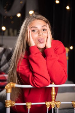 Pijamalı genç bir kadının portresi yatağın arkasında dilini dışarı çıkarıyor. Yüksek kalite fotoğraf