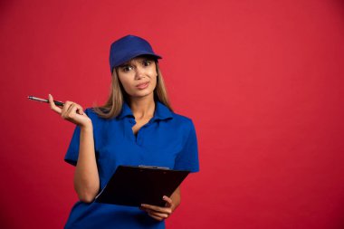 Mavi üniformalı düşünceli bir kadın elinde not panosu ve kalemle poz veriyor. Yüksek kalite fotoğraf