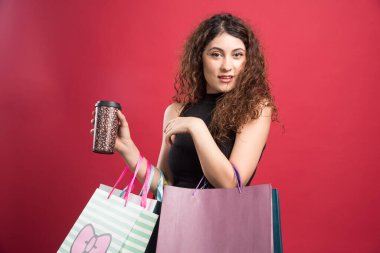 Bardaklı kadın kırmızı arka planda alışverişlerini gösteriyor. 