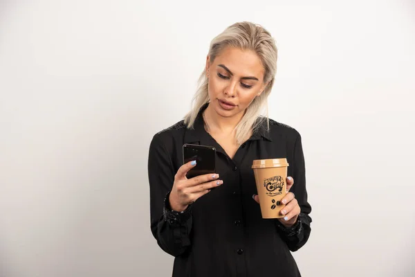Kobieta Patrząc Telefon Komórkowy Trzymając Filiżankę Kawy Wysokiej Jakości Zdjęcie — Zdjęcie stockowe