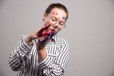 Yüzünde boya ve gri arka planda gözlük olan bir kadın. 