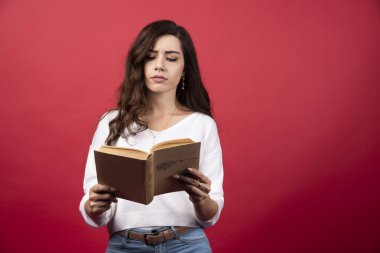 Kırmızı arka planda kitap okuyan genç bir kadın. Yüksek kalite fotoğraf