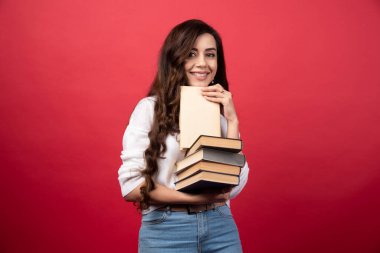 Kitaplar taşıyan ve kırmızı arka planda gülümseyen genç bir kadın. Yüksek kalite fotoğraf
