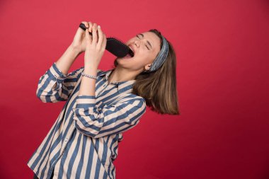 Komik kız kırmızı arka planda siyah saç fırçası kullanarak şarkı söylüyor. Yüksek kalite fotoğraf