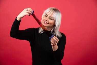 Kırmızı arka planda bir fotoğraf kasetine bakan genç bir kadın. Yüksek kalite fotoğraf