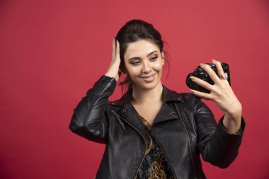 Siyah deri ceketli, elinde profesyonel kamerasıyla selfie çeken havalı bir kız. Yüksek kalite fotoğraf