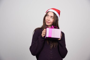 Noel Baba şapkalı düşünceli kadın elinde yaylı bir Noel hediyesi tutuyor. Yüksek kalite fotoğraf