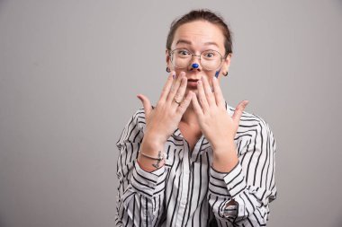 Kadın yüzüne dokunuyor, elleri gri arka planda. 