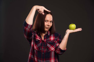 Sonbahar kış koleksiyonu giysileri içinde elinde yeşil bir elma tutan ve onu işaret eden bir kadın model. Yüksek kalite fotoğraf