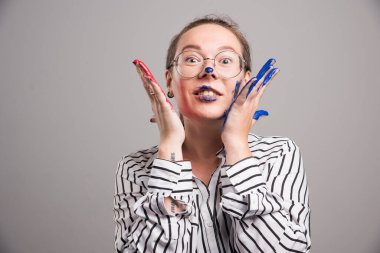 Kadın yüzüne dokunuyor, elleri gri arka planda. 