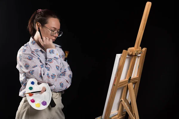 Kobieta Artysta Trzyma Pędzel Patrząc Płótnie Czarnym Tle — Zdjęcie stockowe